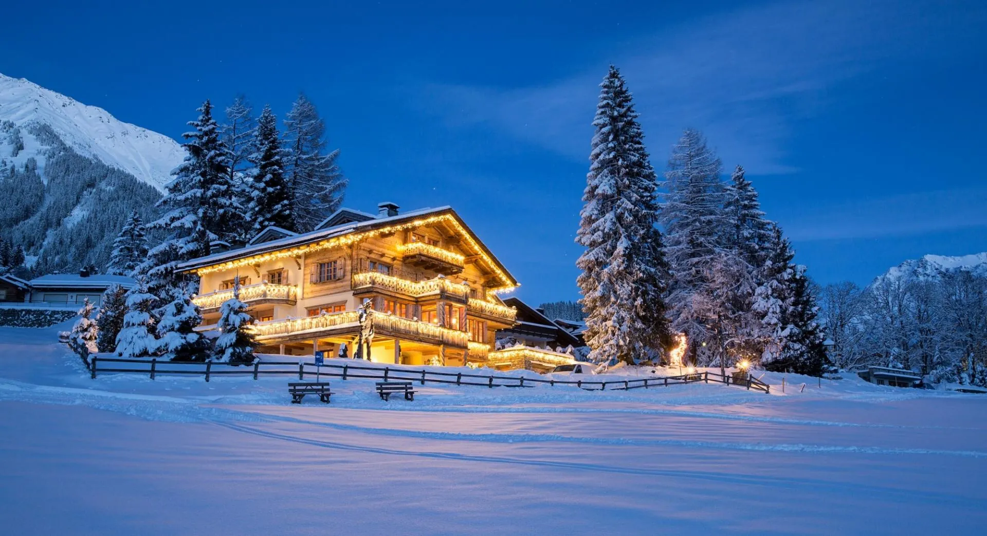 Chalet Kalem across a snowfield at blue hour, with peaks behind, Klosters