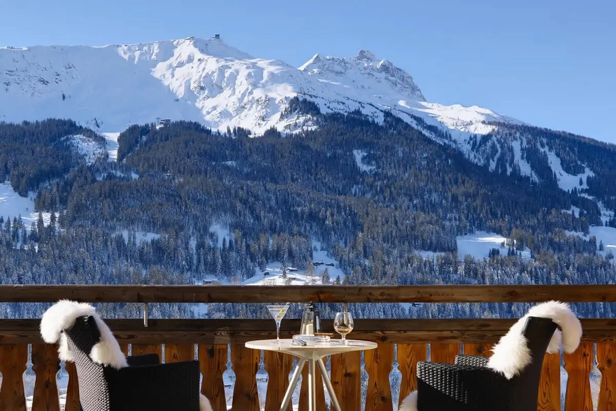 A balcony breakfast table with sheepskins facing snowy peaks at Chalet Kolin, Klosters